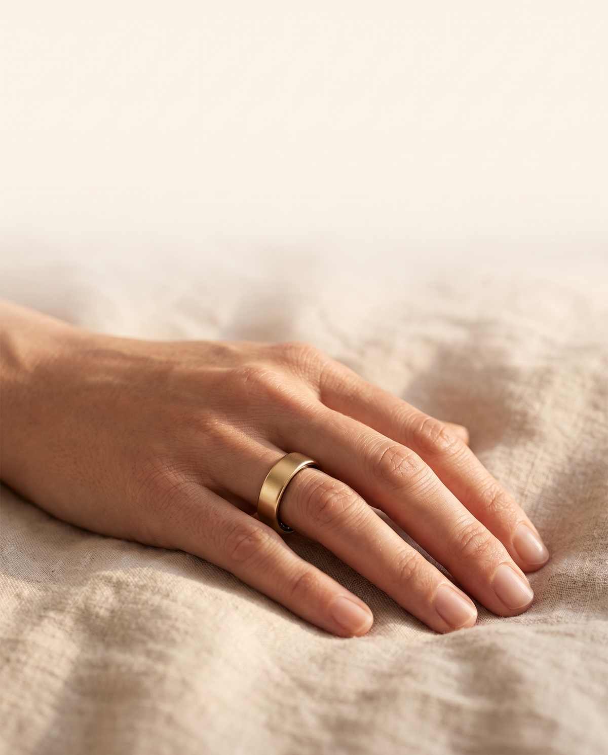 Hand mit HUMANCORE X3 Smart Ring in Gold auf Leinenbettwäsche
